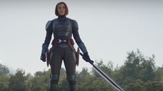 a woman standing on top of a grass covered field holding a giant metal object in her hands