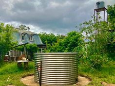 a large metal barrel sitting in the middle of a field next to a house and water tower