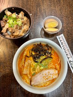 a bowl of ramen with meat and vegetables next to another bowl of soup on a table