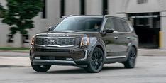 the front end of a brown suv driving down a street next to a tall building