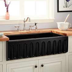 a black sink in a white kitchen with wooden counter tops and cabinets next to a window