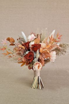 an arrangement of flowers and feathers in a vase on a beige tableclothed surface