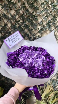 a person holding a bouquet of purple roses with a note on the top that says, it's all wrapped in paper