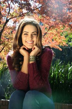 a woman sitting in front of a tree with her hand on her chin and smiling