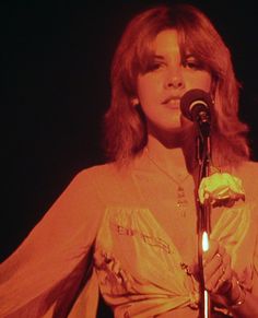 a woman standing in front of a microphone with her hand on top of the microphone