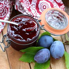 plums and blueberries sit on a wooden table next to a jar of jam