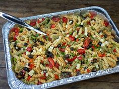 a metal pan filled with pasta salad on top of a wooden table