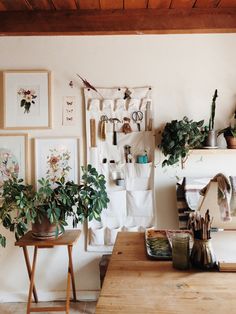 a room filled with lots of potted plants on top of a wooden table next to a white wall