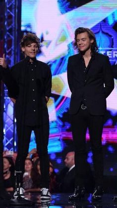 three men are standing on stage at an event and one is wearing a black suit