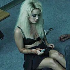 a woman sitting on the floor with blood all over her face and leg, holding a cell phone