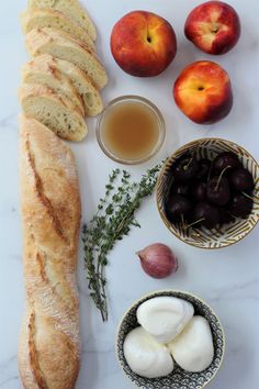 an assortment of bread, fruit and juice on a white countertop with marbleware