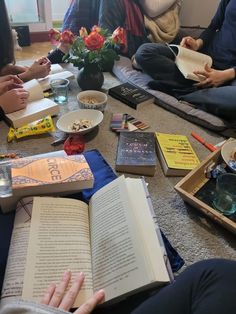 people are sitting on the floor reading books and drinking tea or coffee while one person is holding an open book