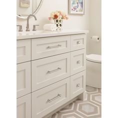 a bathroom with white cabinets and a flower vase on the sink counter next to the toilet