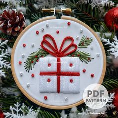 a cross stitch ornament with a red ribbon and present box on it, surrounded by christmas decorations