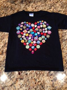 a black t - shirt with colorful buttons in the shape of a heart on it