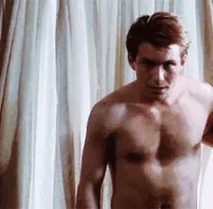 a shirtless man standing in front of a curtain