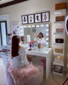 a woman is sitting in front of a vanity with lights on and she is looking into the mirror