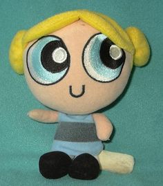 a stuffed doll with big eyes and blonde hair sitting on a green surface, looking at the camera