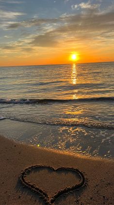 a heart drawn in the sand at sunset