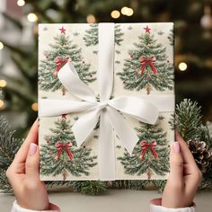 someone holding up a christmas present in front of a christmas tree