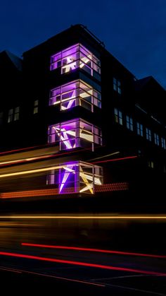 a building that is lit up at night with lights in front of it and cars passing by