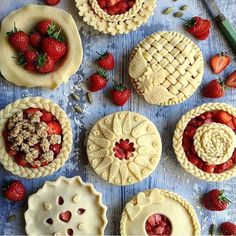 several pies with fresh strawberries and other toppings on a blue surface next to a knife