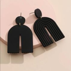 the black earrings are on display against a pink background