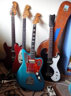 four guitars are lined up on the floor in front of a wall with other instruments