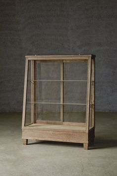 a wooden display case with glass doors on the top and bottom shelves, in front of a concrete wall