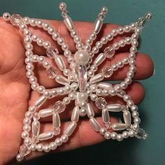 a hand holding a beaded brooch in the shape of a snowflake