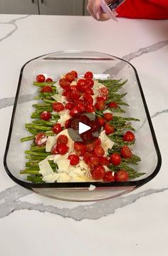 a glass dish filled with tomatoes, cheese and asparagus on top of a table