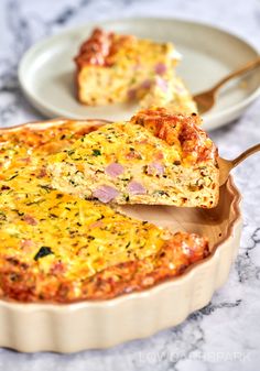 a quiche with ham and cheese in a pie dish on a marble counter top