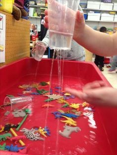 a child's hand pouring water into a plastic container filled with toys