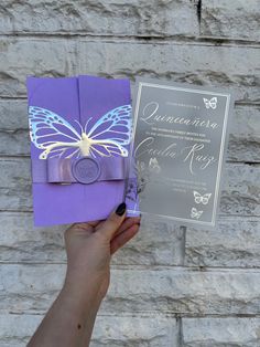 a person holding up a purple and silver wedding card with a butterfly design on it