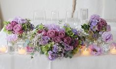 flowers and candles are arranged on the table for an elegant centerpiece in purple tones