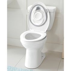 a white toilet with the lid up in a small bathroom area next to a blue and white rug