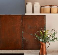 some flowers are in a copper pitcher on the counter next to an old metal cabinet