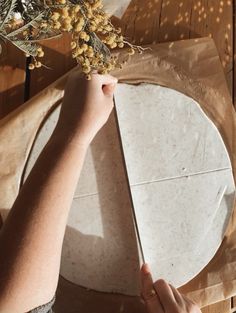 a person is making a pizza on a wooden table with some dried flowers in front of it