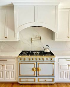 a white and gold stove top oven in a kitchen with wooden floors, cabinets and cupboards