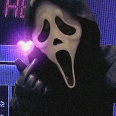 a person wearing a ghost mask and holding a cell phone in their hand with the light on