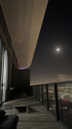 the moon is shining brightly in the night sky over an apartment balcony with black furniture