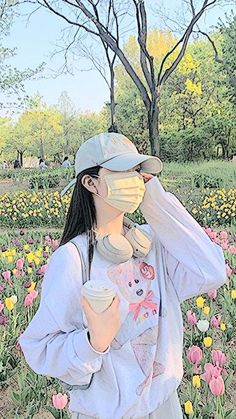 a woman wearing a face mask standing in a field of flowers with a cup of coffee