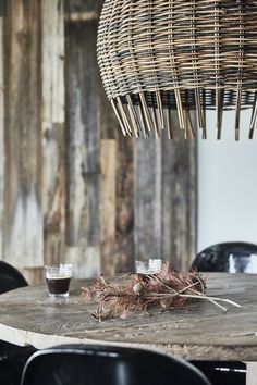 a wooden table topped with two cups filled with liquid next to a wicker light fixture