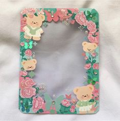 a teddy bear photo frame with pink roses and green leaves on the border, in front of a white background