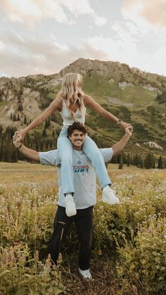 a man carrying a woman on his back in the middle of a field with mountains in the background