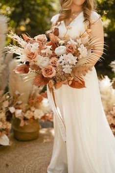 a woman in a white dress is holding a bouquet with flowers and feathers on it