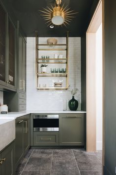 a kitchen with green cabinets and white tile flooring is pictured in this image, there are shelves on the wall above the stove