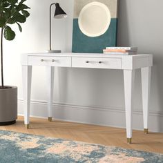 a white desk with two drawers and a plant on it next to a blue rug