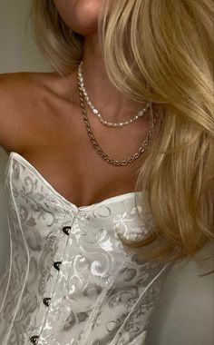 a woman with blonde hair wearing a white corset and pearls on her necklace