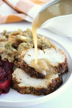 a plate with meat, fruit and stuffing being drizzled on top of it